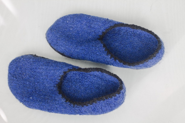 a pair of knitted and felted slippers, quite plain, blue with a black crochet border on top