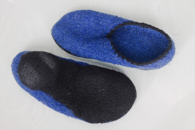The same slippers, one is turned upside down to show the black felted sole, with a raised round area at the heel.