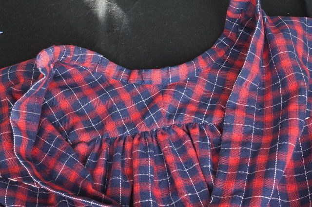 The yoke and collar of a shirt in tartan flannelin red, blue and white; the back is gathered to the yoke