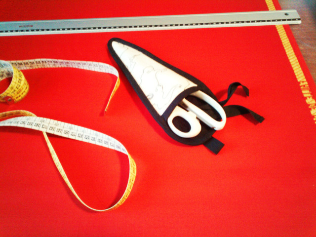 red wool laid on a table with fabric scissors, tailor's tape and a 60 cm metal ruler