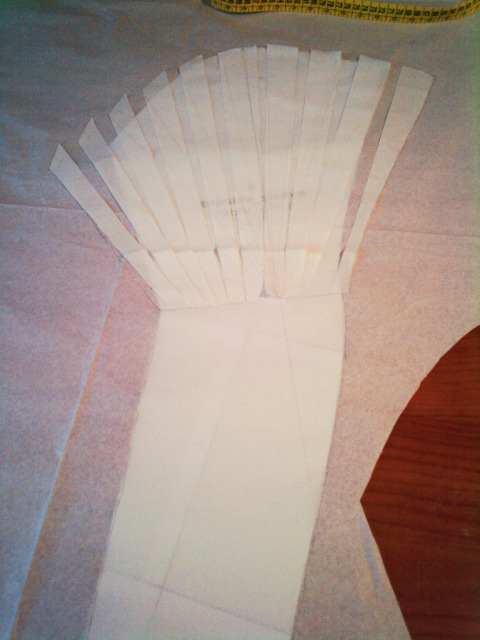 a paper pattern of a sleeve in the process of being widened at the top: the basic sleeve is at the bottom, then there is a sheet of semitransparent tissue paper on top, and the pieces from another copy of the top half of the sleeve spread out on top.