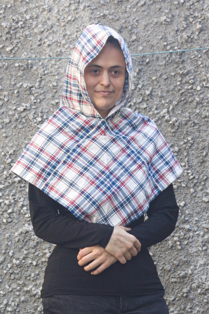 A woman wearing a hood in the same shape, but made in tartan-print flannel. It looks slightly smaller than the linen one.