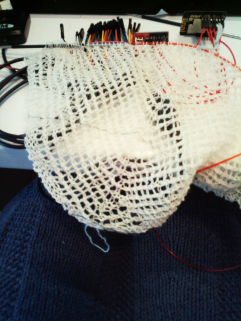 unfocused picture of the beginning of a knit lace shawl on top of some microcontroller boards and a lot of jumper cables