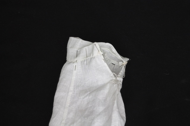 a 2 cm cuff pinned to a gathered sleeve, in the process of being hemstitched to it. Everything is white linen on a black background.