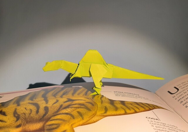 Spinosaurus in origami che passeggia su un libro aperto alla pagina che lo riguarda.