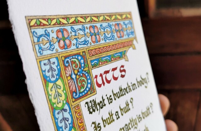 An angled view of an illustrated border around some calligraphy, showing the metallic gold inks catching the light, and the fine white detail inside the coloured patterns.