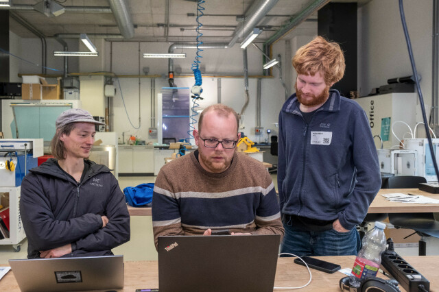 three people in workshop in front of two laptops