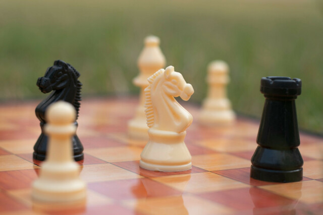 Chess board with a white horse pawn in between a black horse and a black tower.
