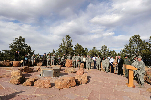 A group of people in military fatigues around a small modern stone circle made of stones about 50 cm high. A man addresses the group from a podium to the right. Falcon Circle USAF College from Wikimedia Commons