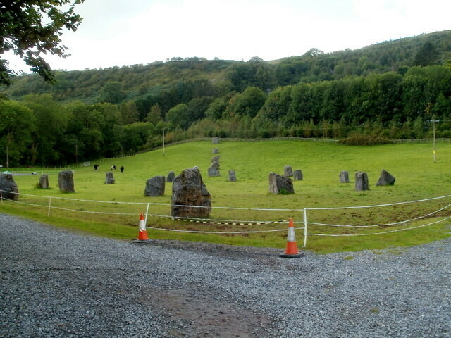 A group of stones arranged in a circle in a green field with woods behind. One of several modern stone circles at Dan yr Ogof show cave. Picture by Jaggery on Geograph.