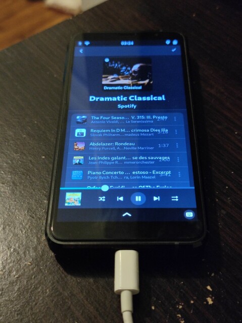 Librem 5 on a wooden table using Spotify via the Spot app, playing the "Dramatic Classical" playlist