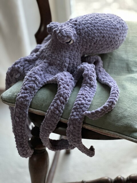 A large grey crochet octopus sitting on a chair. 