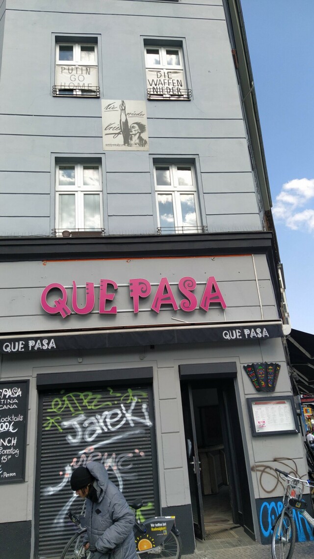 Una facciata di Kreuzberg: messaggi sovrapposti e multilingue. Que Pasa. Nie mehr Krieg, Putin out, die Waffen nieder