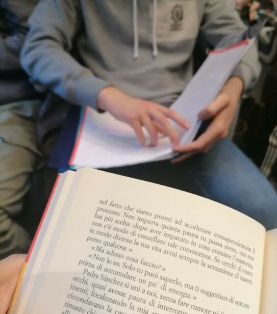 Il libro, aperto sulla pagina che sto leggendo, mentre sono seduta in treno tra altri pendolari. Seduto di fronte a me, senza viso per tutelarne la privacy, un ragazzo che sta ripassando leggendo il suo quaderno di appunti.