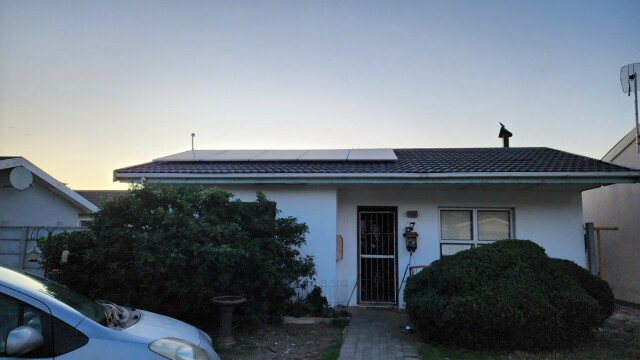 View of the front of our house, wher five big solar panels can be seen stretching from the left side to just past the middle of the roof