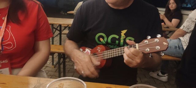 Guy playing ukulele with a QGIS t-shirt 