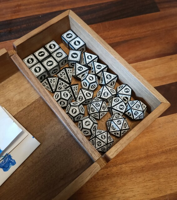 Brown walnut dice tray with a dice compartment full of black and white polyhedral dice.