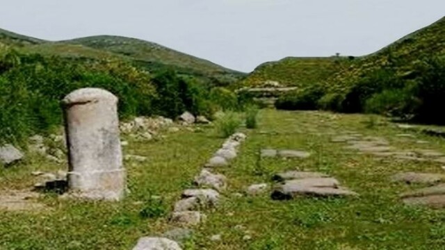 Antica strada, ormai invasa dall'erba, tra verdi colline. Sulla sinistra, una pietra miliare.
Immagine dal web.