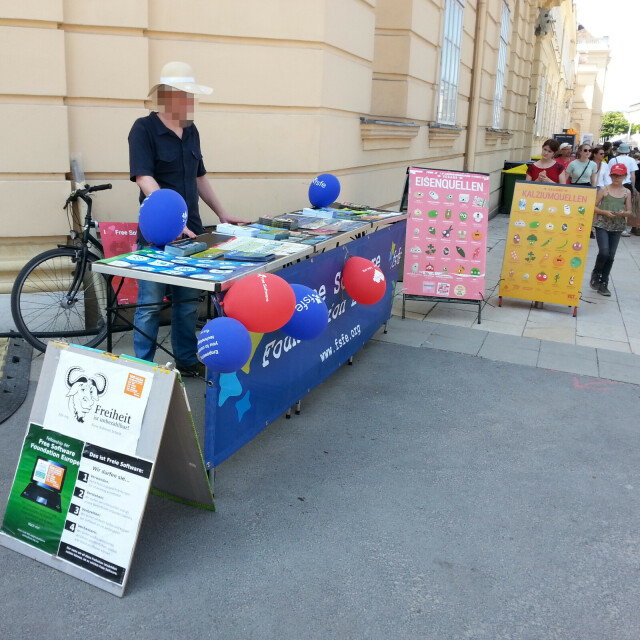 Picture showing a FSFE booth with balloons, posters and a table with FSFE stickers and flyers