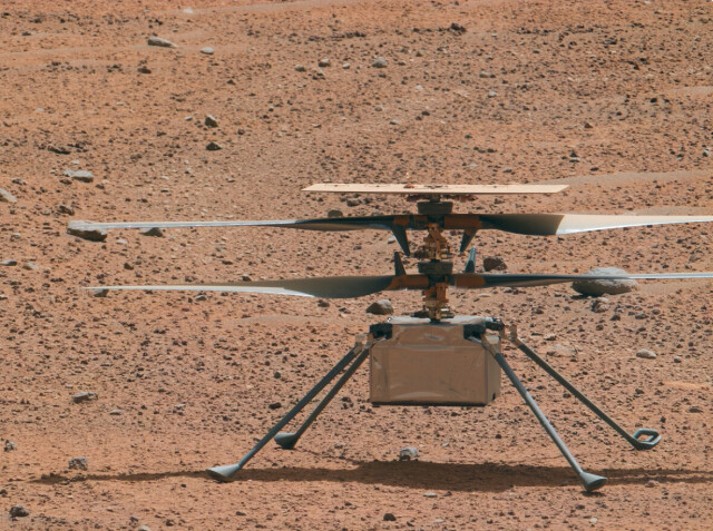 Telephoto picture of the Mars Helicopter Ingenuity on the surface of Mars. The two rotors have accumulated substantial amounts of dust near the rotor shaft. The leading edges are mostly clear of dust, but a fine layer is also apparent on the topside of the rotor. The solor panel also looks dusty. 