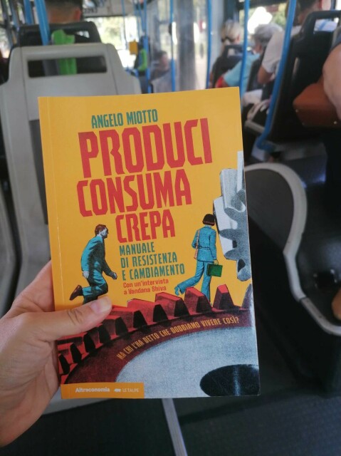 Il libro di Angelo Miotto "Produci consuma crepa - manuale di resistenza e cambiamento" in mano mia, mentre viaggio in autobus.