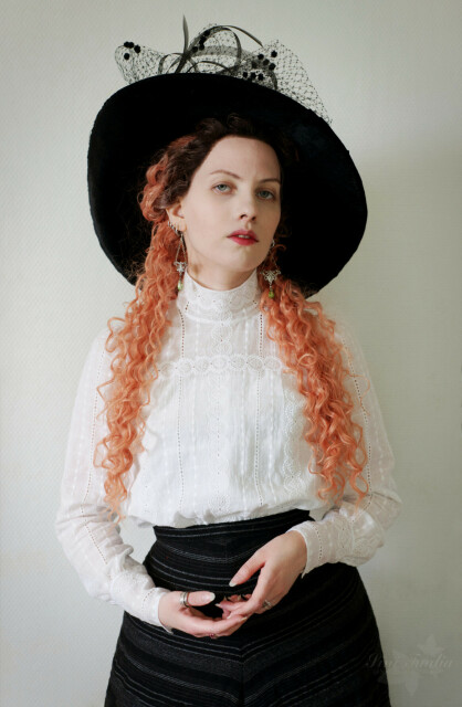 Portrait of the same, but with Sini facing to the front and gazing at the viewer. The light is quite pretty. The front yoke of the blouse has been sewn in a way that looks seamless, with one repeating pattern of the embroidery running across the yoke seam, without any visible seams. The high collar has been made likewise. The hat has some nice dotted veiling and Sini is wearing a curly orange wig, which covers up some of the blouse, but the portrait itself is lovely.