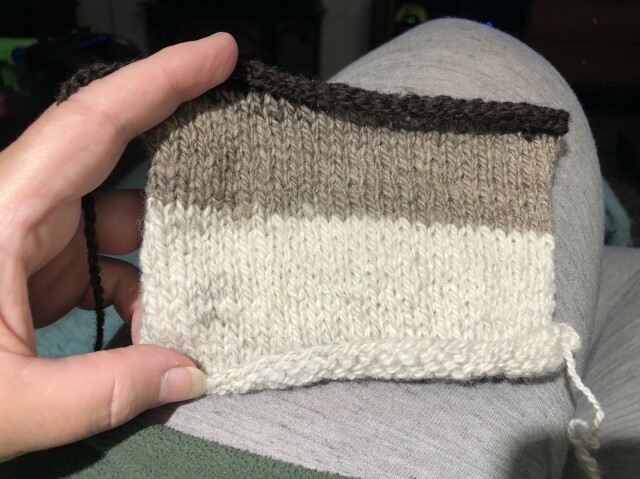 A handknitted swatch about 5” wide by 4” tall, in shades of off-white, grey-brown, and dark brown.