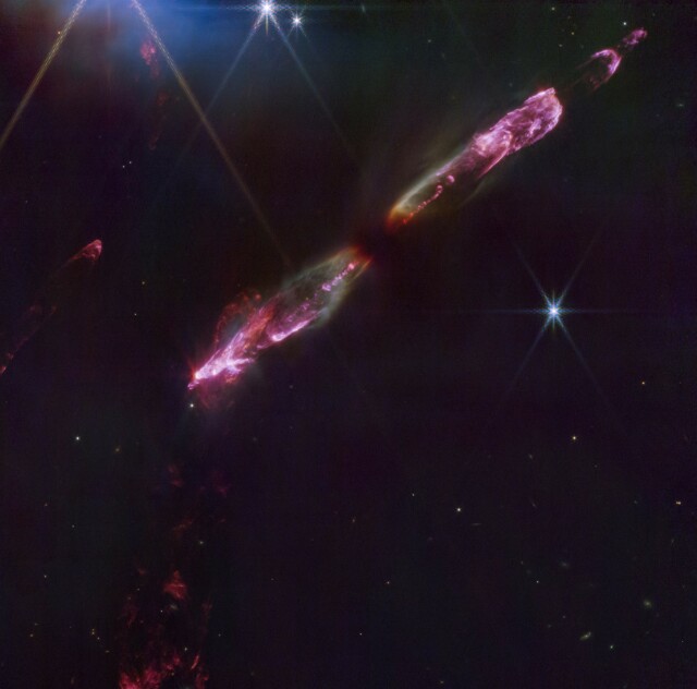 The protostellar outflow HH211 near the IC348 cluster in Perseus as imaged with JWST in the near-infrared (2-5 microns). The linear jet is purple and red due to shocked molecular hydrogen emission, with contributions also from carbon monoxide. There is some green reflection nebulosity along the flanks of the outflow, while the driving protostar is invisible at the centre. There are a few stars and some other molecular hydrogen emission strewn across the dark background.