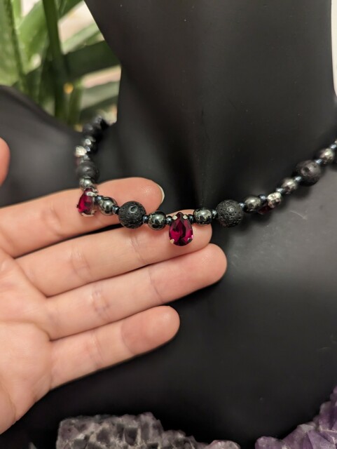 Hand showing handmade necklace with grey black beads and glass red drop pendants on a black doll