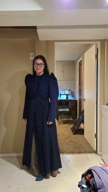 A woman standing awkwardly wearing a navy robe with poofy shoulders.