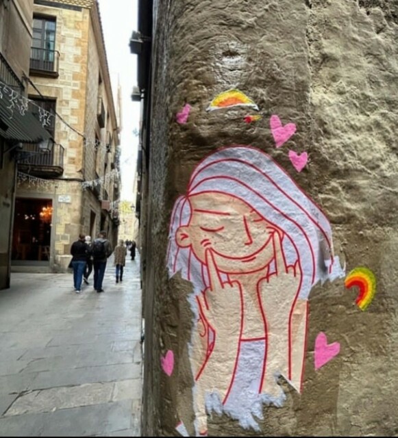 Streetartwall. On the corner of an old house wall in a narrow alley is a small sticker with a drawing of a girl with pink hair, pulling up the corners of her mouth with her middle finger to smile. Around her are little pink hearts and rainbows. A minimalist but very charming little wall mural.