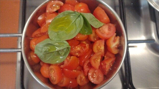 Foto di un pentolino contenente pomodorini freschi tagliati a pezzettini e foglie di basilico. Sul fuoco pronto a diventare un sughetto vitaminico