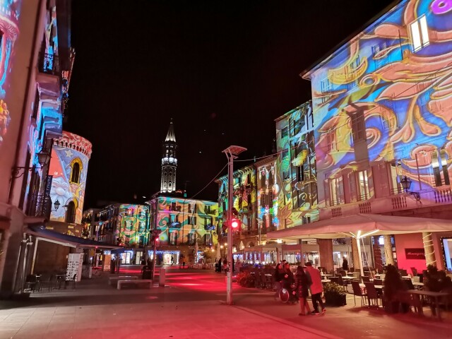 piazza, le case intorno sono illuminate di colori, sullo sfondo il campanile anch'esso illuminato