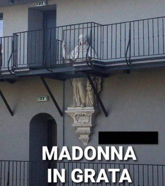 La foto di una statua della madonna parzialmente coperta da una balconata con grata in metallo, tale da sembrare in prigione.