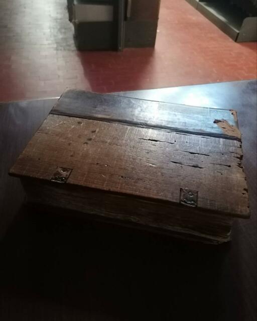 Un libro, con copertina in legno e cuoio, posato su una scrivania nel deposito archivistico.