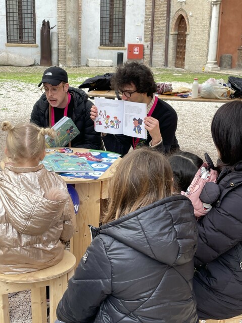 Dario and Tommi from FSFE reading the book, and the back of kids listening to the story