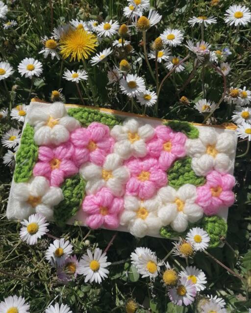 L'astuccio, coperto di fiorellini a cinque petali bianchi e rosa e di foglie verdi, poggiato su un prato tra le margherite