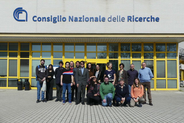 foto di gruppo davanti alla Biblioteca Dario Nobili del CNR di Bologna. Una ventina di persone in posa davanti alla facciata a vetrate e infissi gialli, in alto una parte del muro a piastrelle bianche con la scritta in blu Consiglio Nazionale delle Ricerche