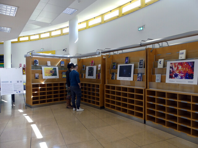 Teche nel corridoio circolare della biblioteca, due persone osservano le foto vincitrici circondate da alcuni libri a tema.