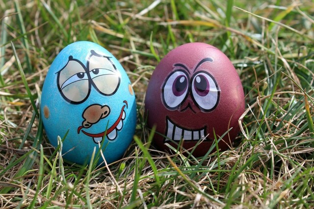 Two eggs laying on grass. The leftmost is painted in light blue and it has a weird expression, the rightmost has a happy expression and it’s painted in dark red