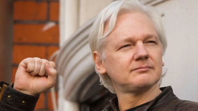 Un homme aux cheveux blancs (Julian Assange) lève le poing.