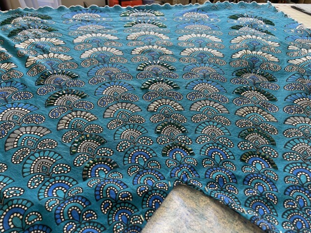 Wide angle view of azure colored kaftan with a fan design motif laid flat on a table to show off the rows of blue and silver beads running from neckline to hem. 
