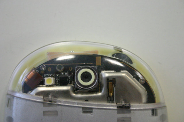 Top part of the back of the phone's casing, featuring a round asymmetrical design with transparent plastic showing the phone's PCB around the camera sensor.
