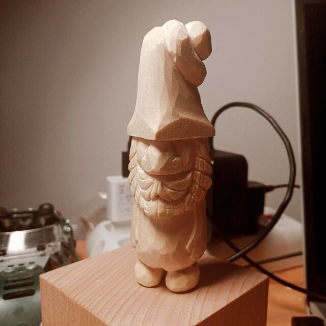 Un piccolo gnomo di legno intagliato. Naso grande, barba folta e cappello strano.