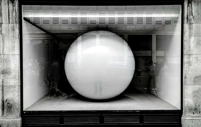 Black and white photo of a giant white ball in a shop window, looking like an eye.