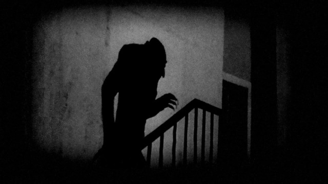 An iconic, monstrous, black and white photo of a shadow on the wall, climbing the stairs with an extended arm, from Friedrich Murnau's incredible Nosferatu  (1922)