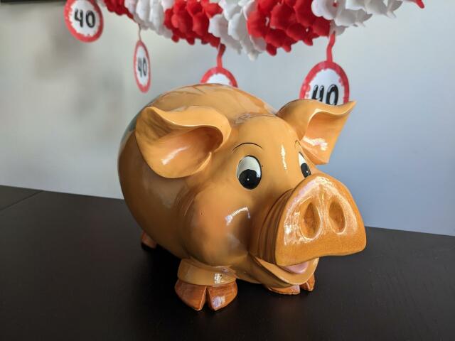 Brownish- yellowish piggy bank. In the background you can see a red and white garland with the number 40