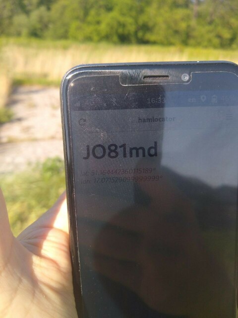 Photo of a PinePhone running my application called "hamlocator", showing a current Maidenhead locator: JO81md. Some greenery in the background.