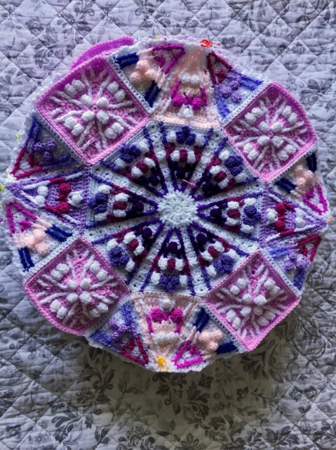 Close up of one of nine circles made of many crochet pieces sewn together. There is an octagon in the center with squares and sets of 3 triangles on alternating sides. It looks a bit like stained glass with the different colored pieces.