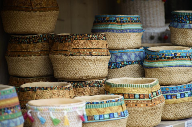 Stacks and rows of woven baskets, all with different patterned fabric borders around the openings, in browns and blues